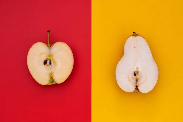 Apple vs Pear. Half apple on red background and half pear on yellow background top view.