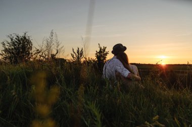 Genç adam ve birlikte çimenlerin üzerinde oturan ve arkadan fotoğraflandı gündoğumu izlerken kadın.
