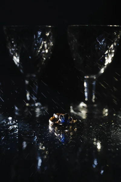 Wineglasses and the ring with blue diamond under water droplets.