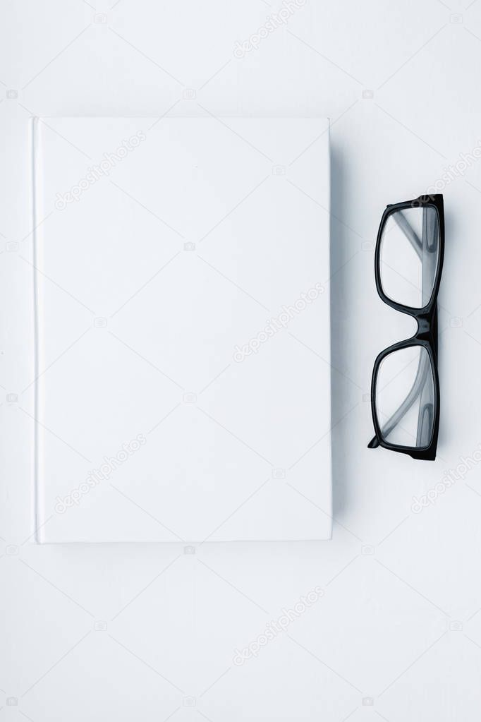 Notebook and eyeglasses on the white table.