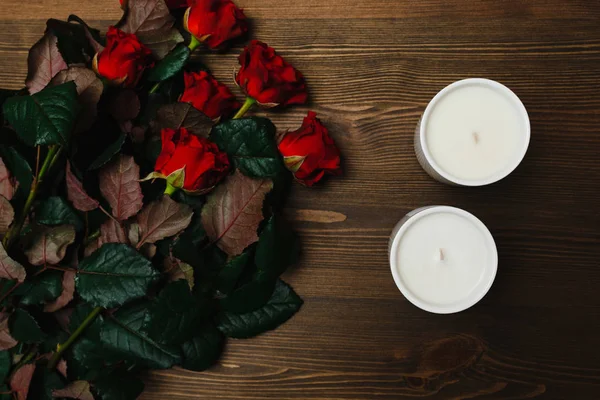 Red roses and white candles on the wooden surface