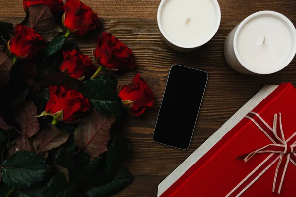 Red roses, smartphone, candles and gift box on the wooden background