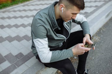 Genç adam kaldırımda oturan ve onun Smartphone kullanarak