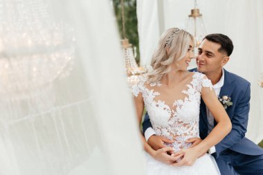 Oturan gelin ve damat birbirlerine bakıp gülümsüyor. Mutlu yeni evliler. Yeni evlilerin portresi. Düğün fotoğrafçılığı