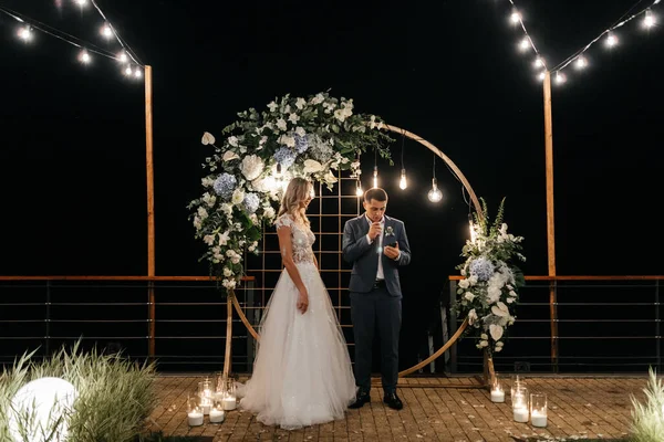 Handsome man saying an oath to the bride from the phone and standing near the circle wedding arch. Newlywed portrait. Wedding photography