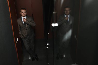 Bej renkli damalı takım elbiseli, kravatını düzelten ciddi bir adam. Damat portresi. Erkek portresi