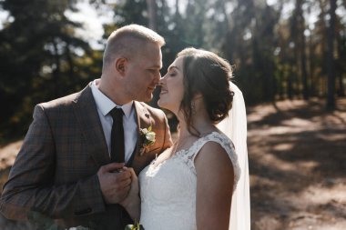 Ormanda gülümseyen gelinini öpecek damat. Öpüşmeden önce bir dakika. Gelin ve damat portresi. Düğün fotoğrafçılığı