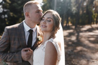 Damat, gelini el ele tutuşurken öpüyor. Gelin ve damat portresi. Düğün fotoğrafçılığı