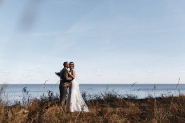 Groon, denizin arka planında gülümseyen gelini öpüyor. Gelin ve damat portresi. Yeni evlilerin portresi.