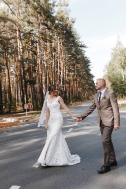 Gelin ve damat çam ağaçlarının arasında yola çıkıyorlar. Gelin ve damat portresi. Düğün fotoğrafçılığı