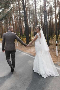 Gülümseyen gelin ve damat ormanda yolda giderken arkadan fotoğraflandı. Gelin ve damat portresi. Düğün fotoğrafçılığı