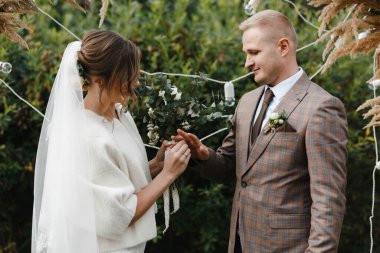 Gelin nikah yüzüğünü damadın parmağına takıyor. Gelin ve damat. Düğün töreni. Açık havada düğün töreni.