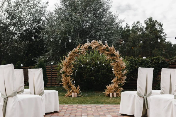 Wedding arch decorated with flowers and lights and chairs for guests. Wedding ceremony. Wedding arch. Wedding ceremony place