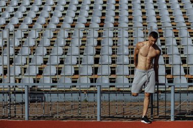 Stadyumda antrenmandan önce bacaklarının ısınmasını sağlayan tişörtsüz bir sporcu. Sporcu. Güçlü adam.