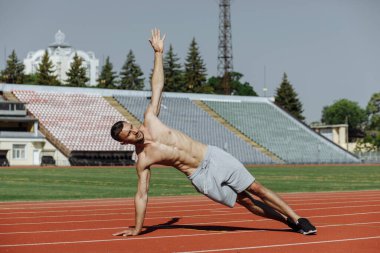 Gömleksiz, kaslı bir adam stadyumda kalas egzersizi yapıyor. Sporcu. Güçlü adam.