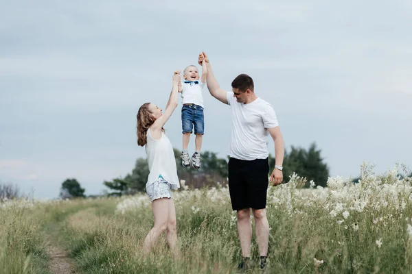 Mother and father lifting their small son up holding his hands while walking on nature. Young happy family. Mother, father and little son. High quality photo