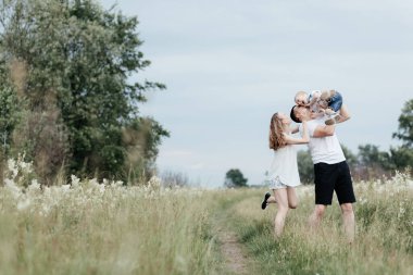 Mutlu gülümseyen ebeveynler yazın doğada oğluyla oynuyorlar. Genç ve mutlu bir aile. Anne, baba ve küçük oğul.