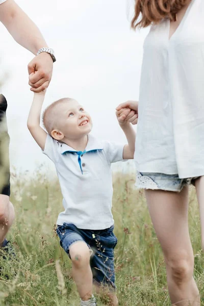 Menino pequeno sorrindo e segurando as mãos de seus pais enquanto caminham sobre a natureza. Família feliz — Fotografia de Stock