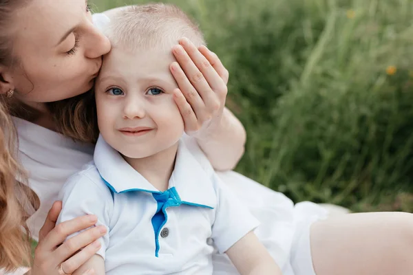 Matka líbá svého malého syna modrýma očima na pozadí hřiště. Matka a syn. Šťastná rodina — Stock fotografie