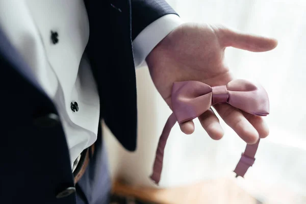 Businessman holding pink bow tie in his hand. Wedding man accessories. Close up