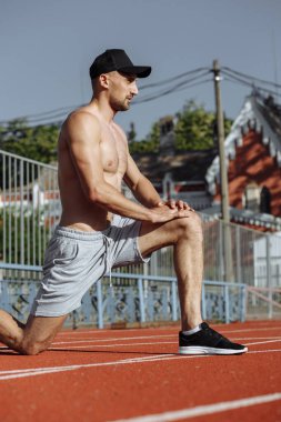 Spor antrenmanından önce tişörtsüz kaslı bir adam ısınıyor. Güçlü adam.