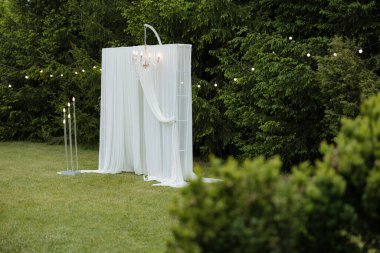 A serene garden features elegant drapes and soft lighting, creating a romantic atmosphere for a wedding ceremony.