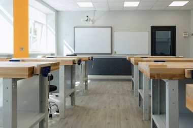 Bright workshop features large wooden desks arranged for creative projects, flooded with natural light from windows.