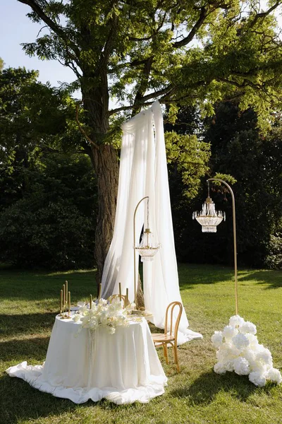 Sersemletici bir açık hava yemek sahnesi yemyeşil bir ağacın altında sergilenir. Yumuşak örtüler, zarif ışıklar ve çiçeklerle süslenir..