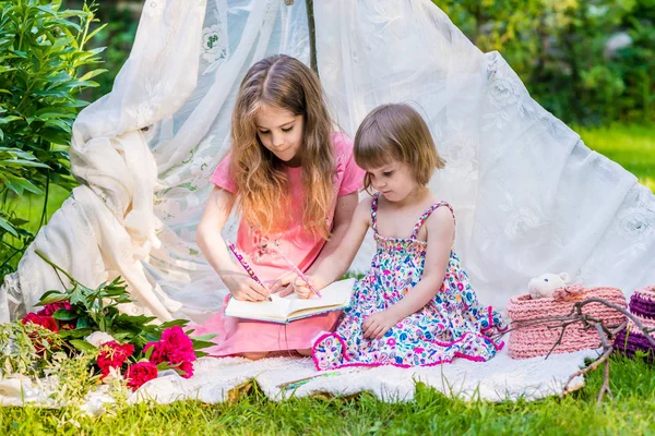 Två systrar i flerfärgade klänningar sitter i vitt boho tält utomhus — Stockfoto
