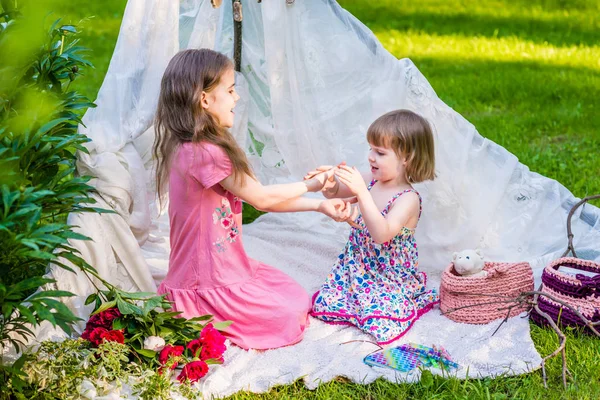 Two sisters in multi-colored dresses sit in white boho tent outd — Stock Photo, Image