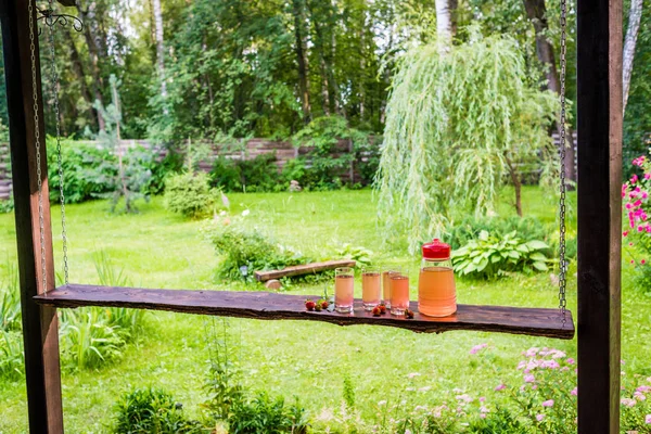 Mesa de madeira longa com quatro copos completos e jarro de suco de frutas — Fotografia de Stock