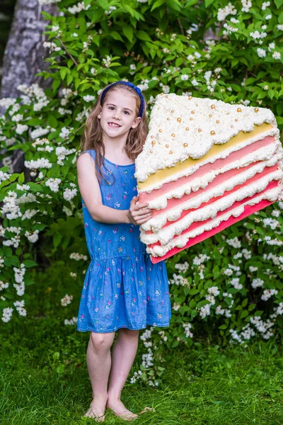 8岁的女孩拿着那块蛋糕。夏季派对户外. — 图库照片