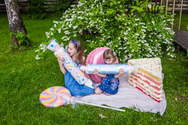 Dos chicas sostienen grandes caramelos falsos y tratan de probarlo. Zona de fotos i —  Fotos de Stock