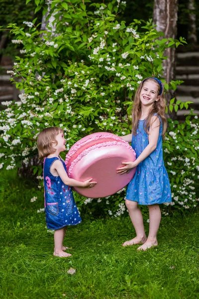 Two girls hold big macarons. Summer party outdoor. — Stock Photo, Image