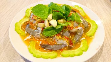 Bu Tay yemeği baharatlı sos ve otlar ile balık sosu taze karides. Otlar dilimlenmiş sarımsak, nane yaprakları ve dilimlenmiş kabak vardır. Ahşap bir masada beyaz bir çanak olarak servis edildi.