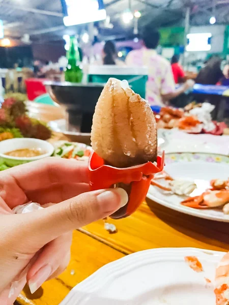 A woman\'s hand is holding a big claw crab which was steamed and peeled out. It has orange color and look like very delicious. This is one of the most popular seafood. Image in blurred background.