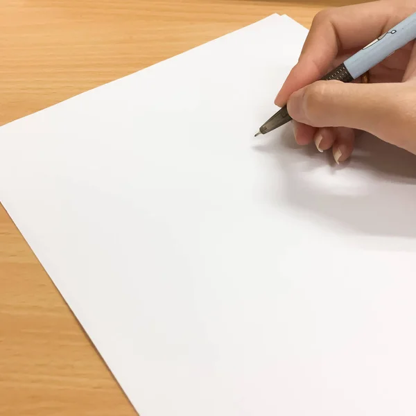 La mano de una mujer es empezar a escribir algo con un bolígrafo negro en un papel blanco. Hay el espacio vacío en el papel que se puede añadir un texto o letras o dibujo . —  Fotos de Stock