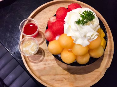 Bu siyah bir fincan mango, kavun ve karpuz ile birlikte buz kar taneleri olan bir karışımı meyve Bingsu olduğunu. Sarı toplar kavun. Kırmızı toplar karpuz. Mangolar platformda kareler vardır