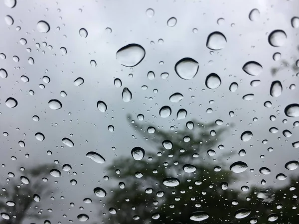 Die Regentropfen auf der Windschutzscheibe oder Windschutzscheibe oder Autoscheibe. Blick aus dem Inneren des Autos mit grauem Himmelshintergrund — Stockfoto