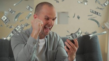 Akıllı telefon kullanan ve spor bahislerinden çok para kazanan bir adam. Kanepede oturan ve yukarıdan para düşerken sevinen adam.