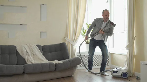 男人在吸尘器上玩就像在吉他上玩一样，在打扫房子的时候玩得很开心 — 图库照片