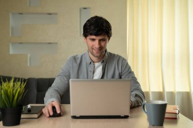 Gülümseyen adam evde çalışırken dizüstü bilgisayar kullanıyor.