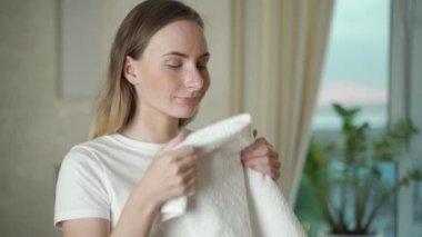 Oturma odasında çamaşırları yıkayan mutlu bir kadın yeni bir çamaşır kokusu alıyor.