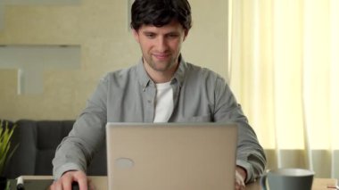 Gülümseyen adam evde çalışırken dizüstü bilgisayar kullanıyor.
