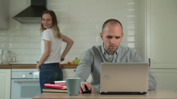 Donna che cucina in cucina e uomo che lavora con il computer portatile a tavola a casa — Video Stock