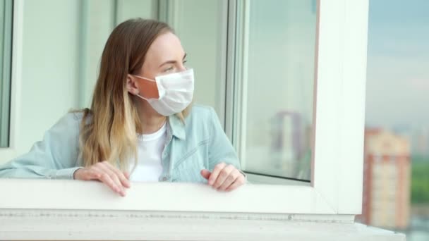 Het meisje verwijdert het medisch masker op het balkon van haar appartement. Een jonge vrouw verwijdert haar masker. — Stockvideo