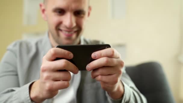 Gelukkig, jonge man speelt spel op smartphone thuis — Stockvideo