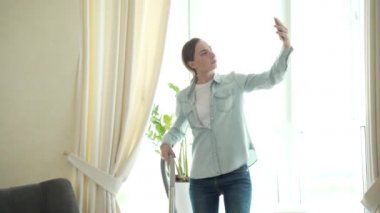 Elinde elektrikli süpürge olan bir kadın evdeki video bağlantısıyla konuşuyor.