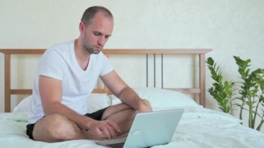 Yatak odasındaki bir yatakta dizüstü bilgisayarla çalışan bir adam için maddi kayıplar.