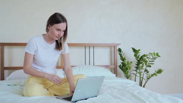 Женщина с ноутбуком, сидя в постели, празднуя успех, онлайн лотереи выиграть, чтение хорошее сообщение, чаты в социальной сети в спальне дома — стоковое видео